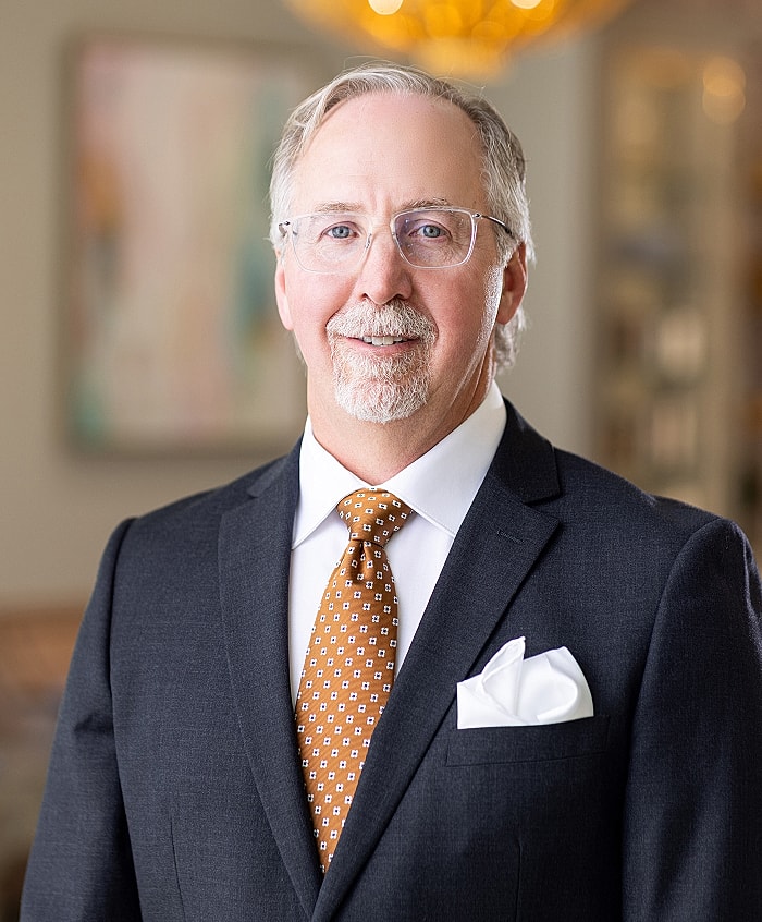 Man in suit with glasses and orange tie.