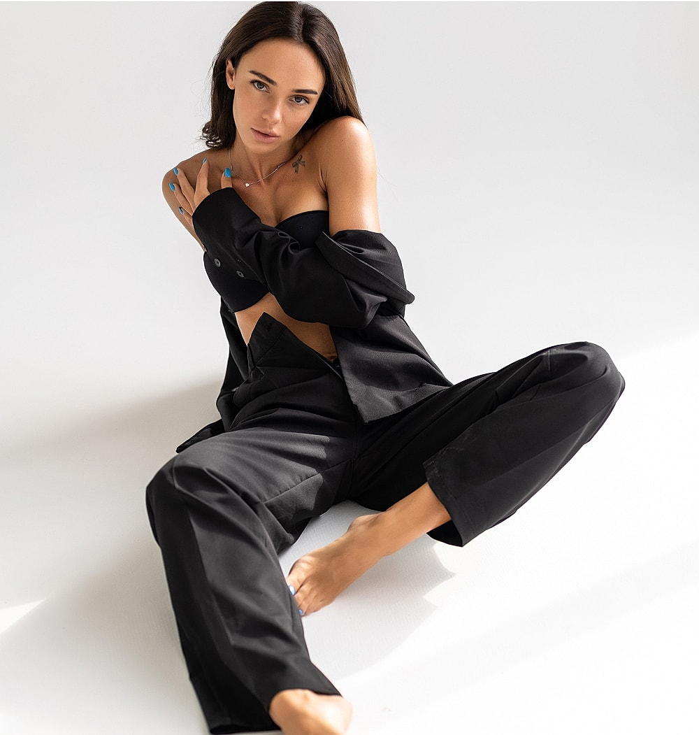 Model in black attire sitting against white background.