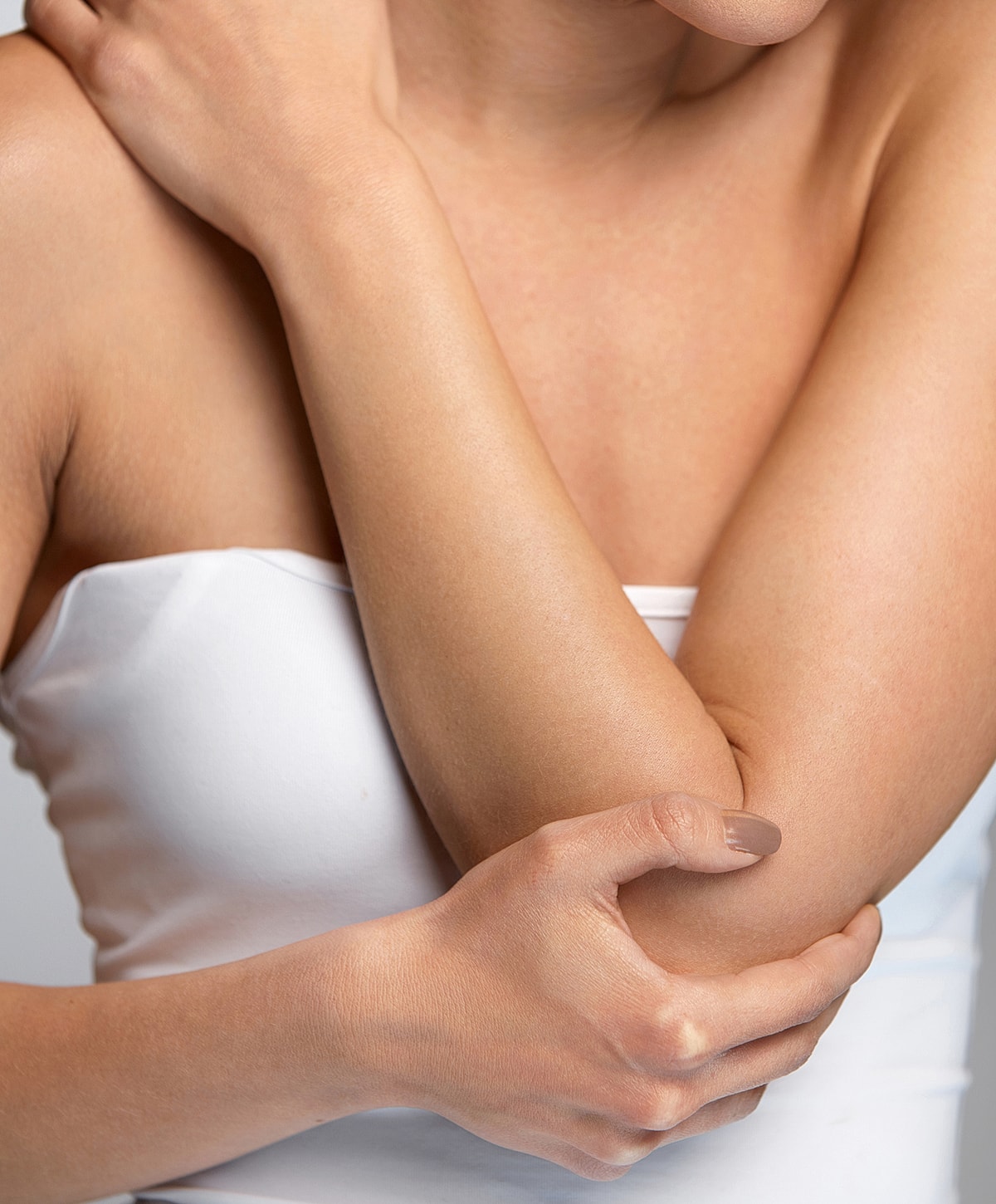 Person holding their arm gently, wearing white top.