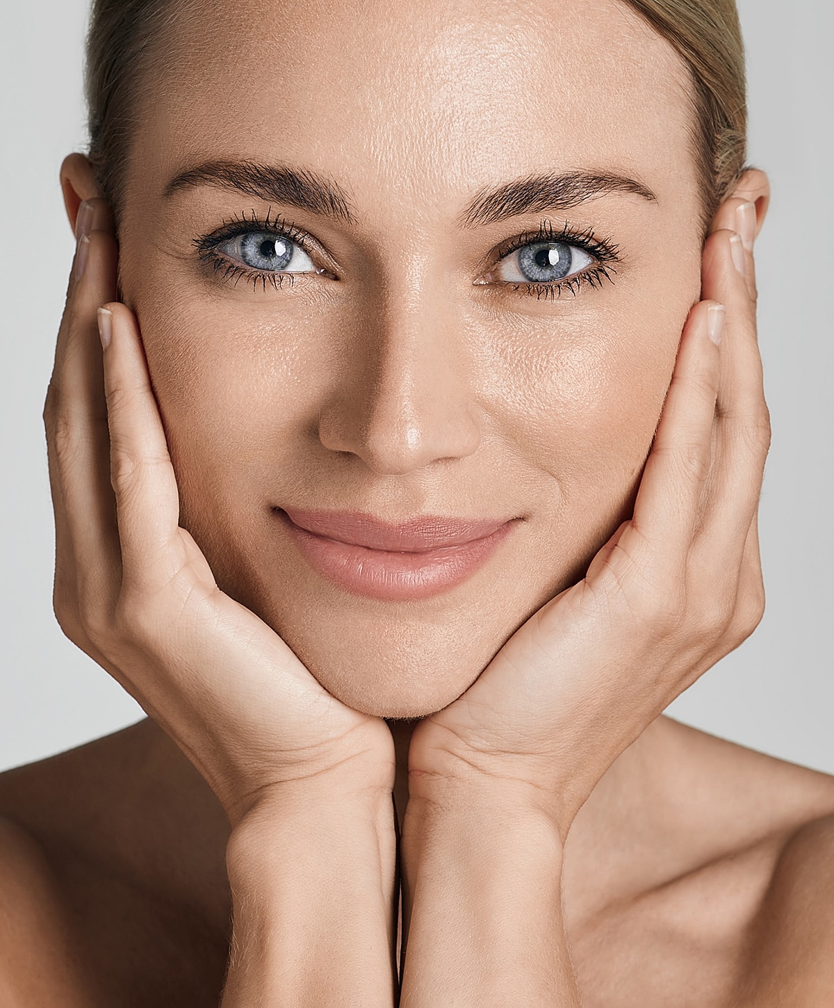 Smiling woman holding face, soft natural lighting.