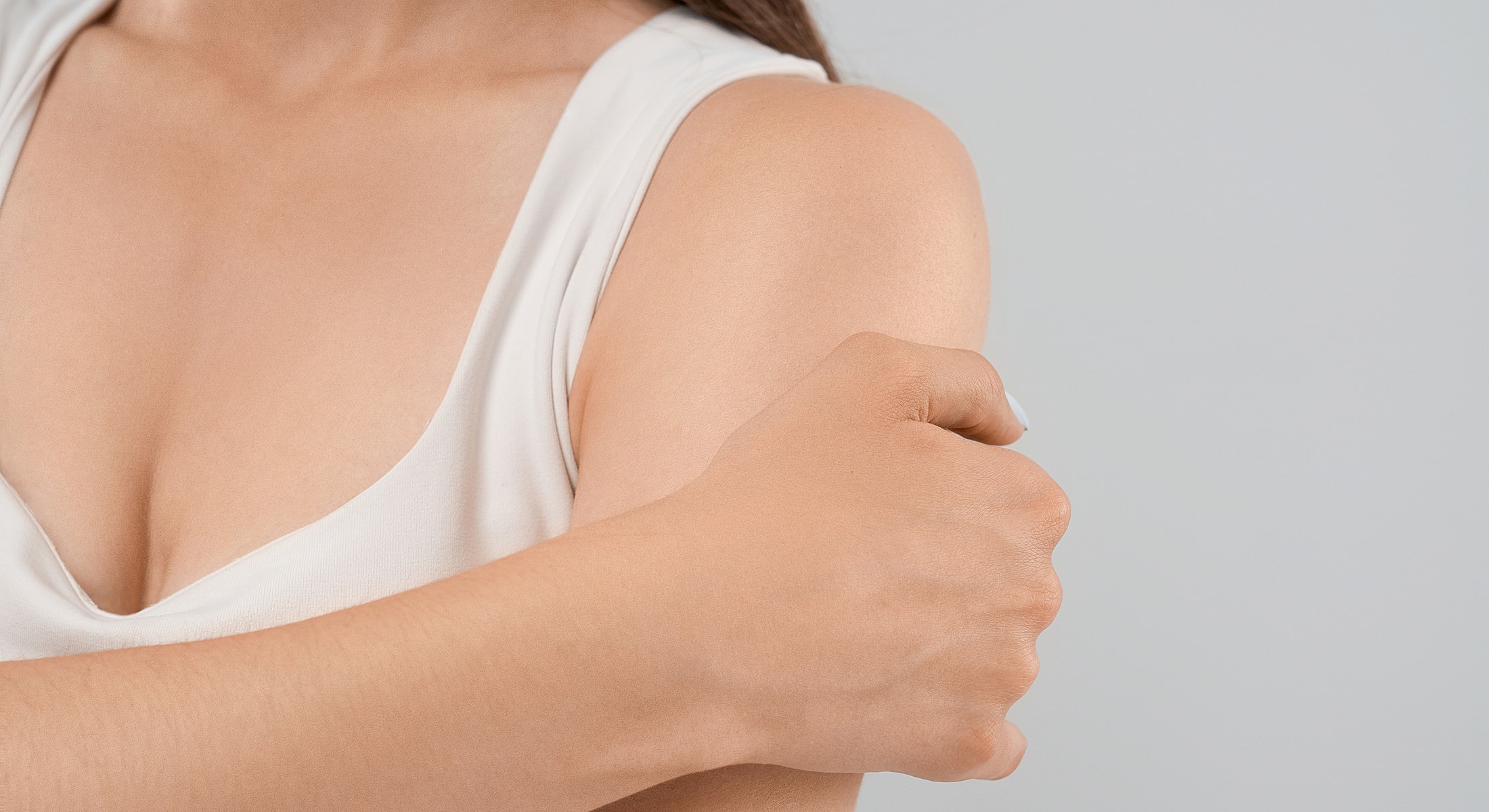 Person holding their arm with a neutral background.